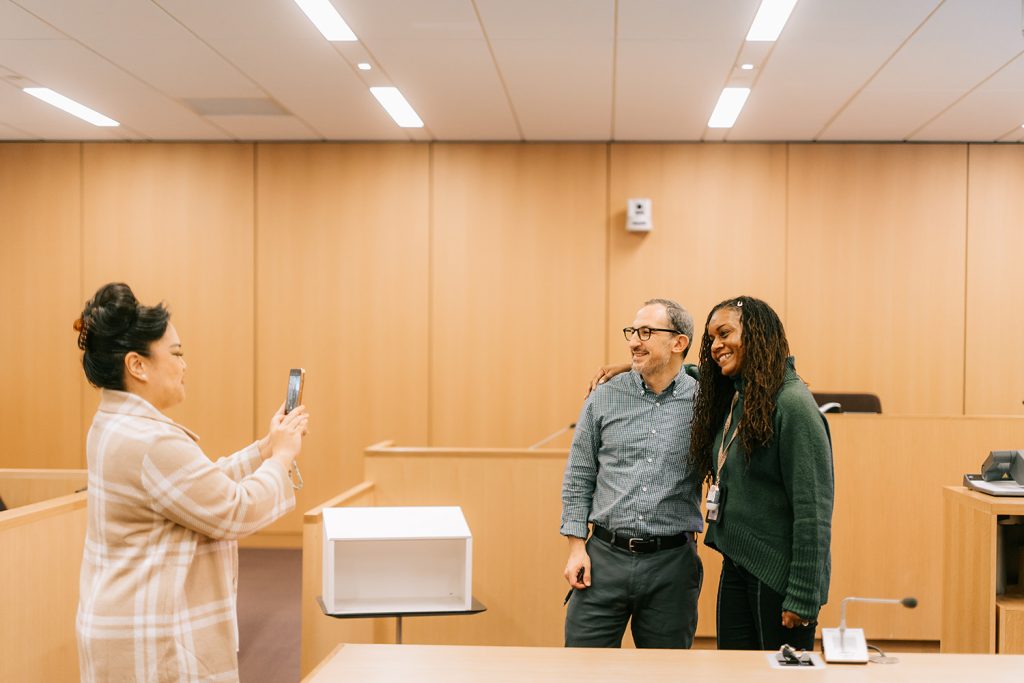woman takes a photo of professor Todd Berger smiling with a student in the courtroom